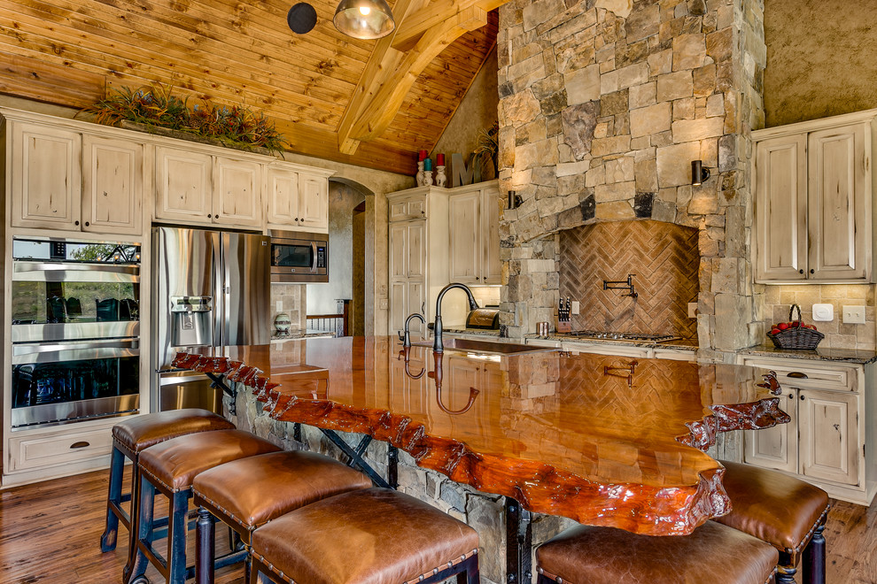 Rustic kitchen in Wichita with a single-bowl sink, raised-panel cabinets, distressed cabinets, brick splashback, stainless steel appliances, medium hardwood flooring and an island.