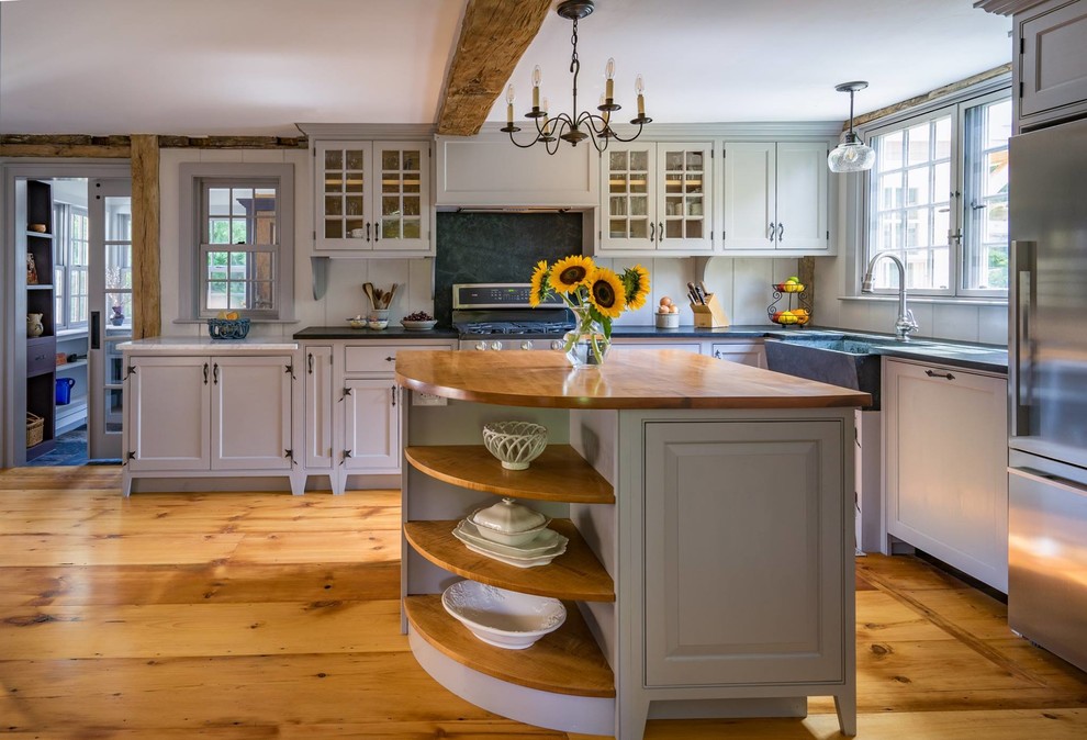 Klassische Küche in L-Form mit Landhausspüle, Schrankfronten mit vertiefter Füllung, weißen Schränken, Küchenrückwand in Weiß, Küchengeräten aus Edelstahl, braunem Holzboden, Kücheninsel, braunem Boden und brauner Arbeitsplatte in Boston