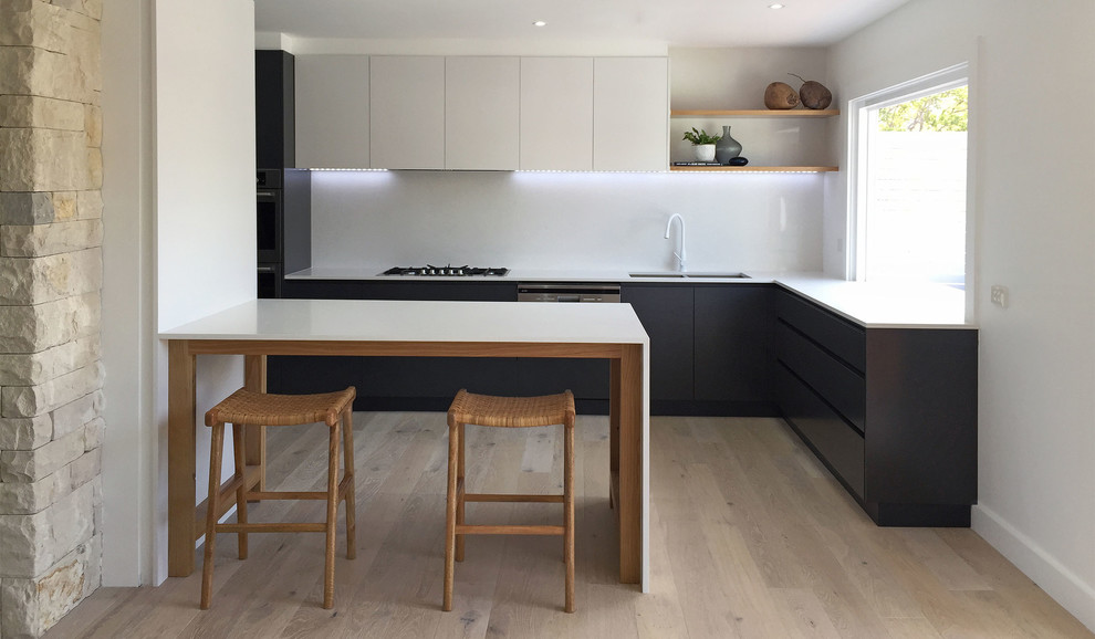 Photo of a medium sized contemporary l-shaped open plan kitchen in Central Coast with a submerged sink, black cabinets, engineered stone countertops, white splashback, stone slab splashback, stainless steel appliances, light hardwood flooring, an island and beige floors.