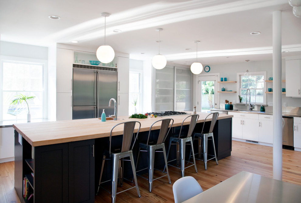На фото: угловая кухня в современном стиле с плоскими фасадами, техникой из нержавеющей стали, обеденным столом, деревянной столешницей и черно-белыми фасадами с