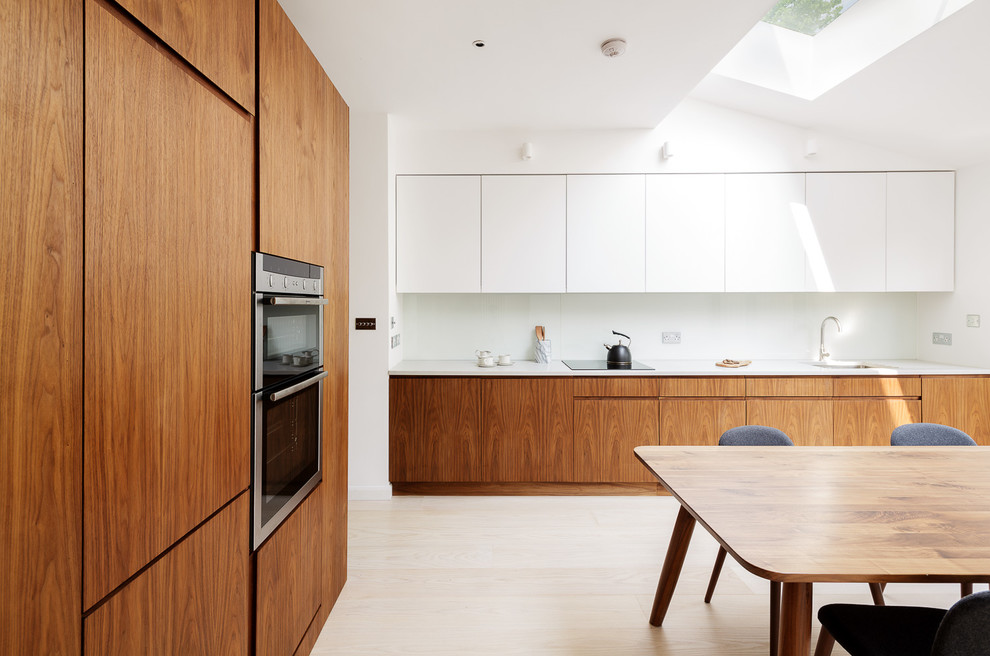 Moderne Wohnküche ohne Insel in L-Form mit flächenbündigen Schrankfronten, hellbraunen Holzschränken und hellem Holzboden in London