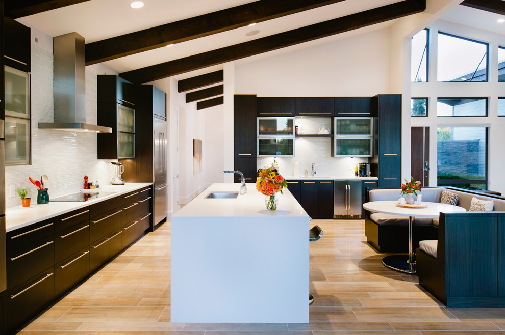 Пример оригинального дизайна: угловая кухня-гостиная в современном стиле с врезной мойкой, плоскими фасадами, темными деревянными фасадами, фартуком из удлиненной плитки и техникой из нержавеющей стали
