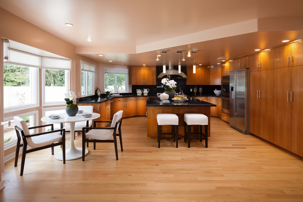 Modern inredning av ett kök och matrum, med släta luckor, skåp i mellenmörkt trä, bänkskiva i onyx, svart stänkskydd, stänkskydd i keramik, rostfria vitvaror, ljust trägolv och en köksö