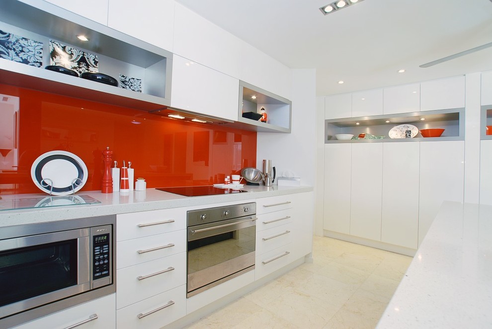 Réalisation d'une cuisine design avec un placard à porte plane, une crédence rouge, une crédence en feuille de verre et des portes de placard blanches.