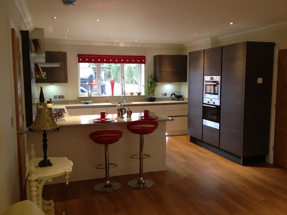 Mid-sized trendy u-shaped medium tone wood floor eat-in kitchen photo in Hampshire with flat-panel cabinets, stainless steel appliances and a peninsula