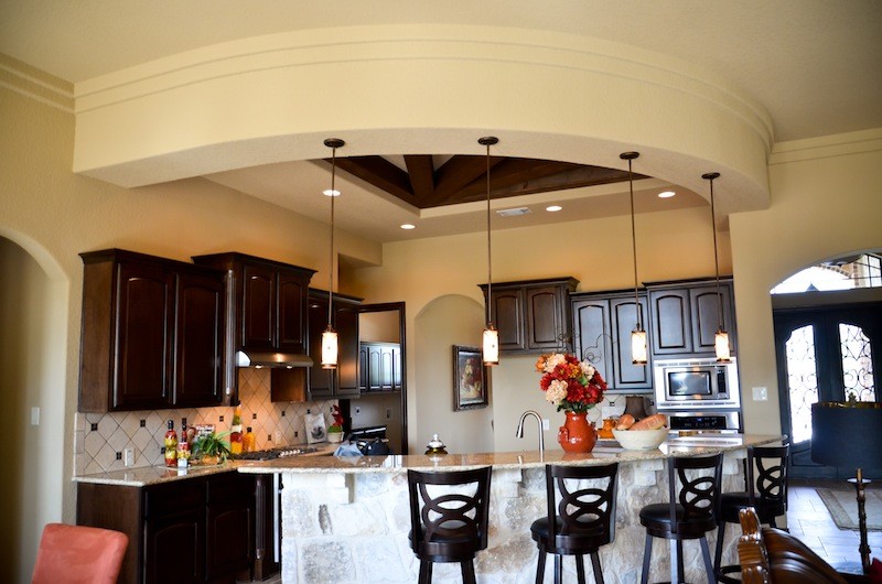 Mid-sized tuscan l-shaped open concept kitchen photo in Austin with raised-panel cabinets, dark wood cabinets, granite countertops, beige backsplash, ceramic backsplash, stainless steel appliances and an island