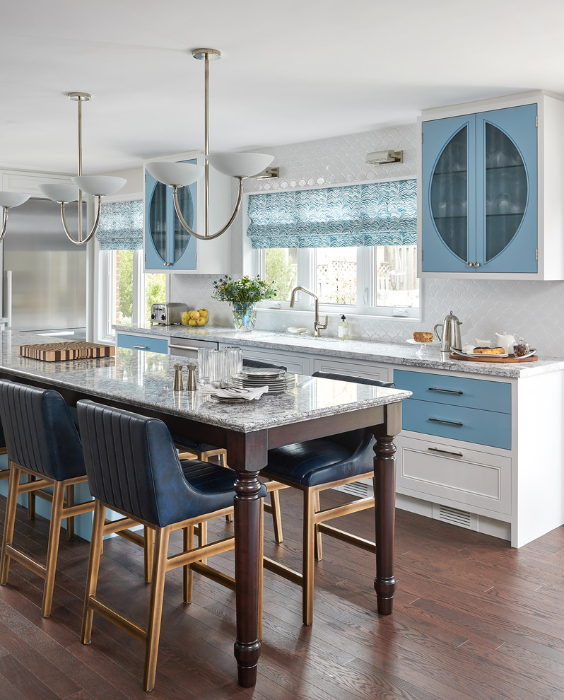 Inredning av ett klassiskt stort kök, med en undermonterad diskho, blå skåp, bänkskiva i kvarts, vitt stänkskydd, rostfria vitvaror, en köksö, brunt golv, luckor med glaspanel och mörkt trägolv