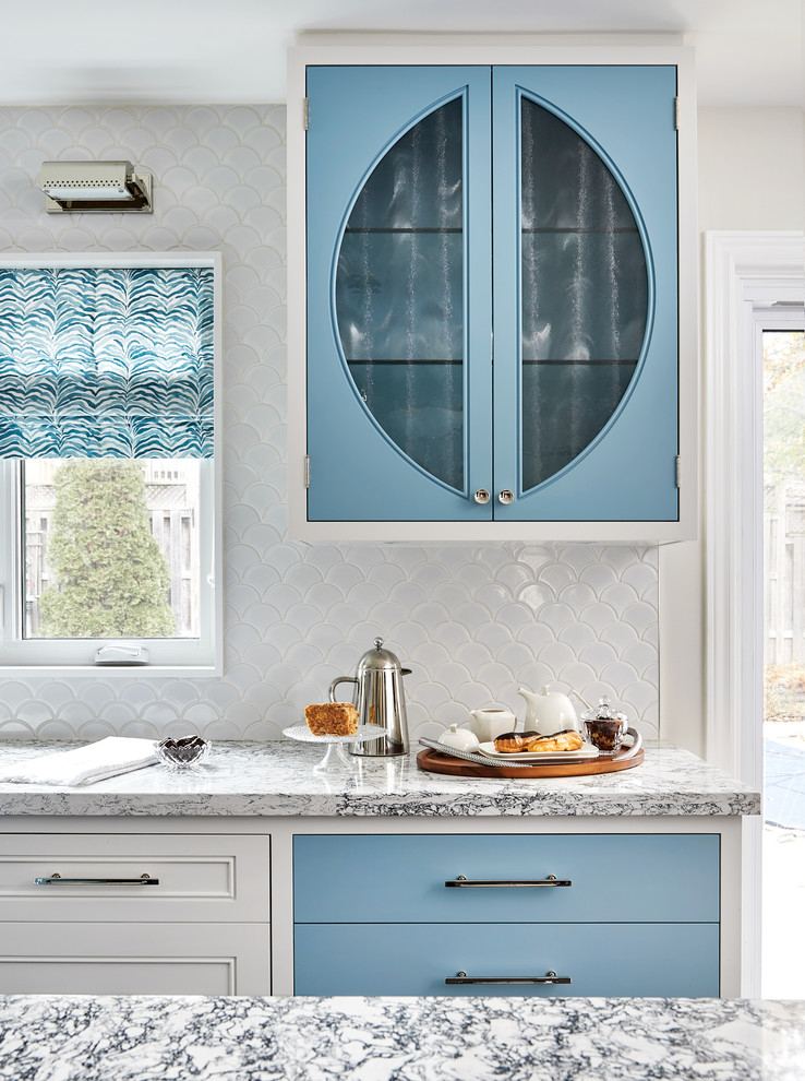 Inredning av ett klassiskt stort blå blått kök, med en undermonterad diskho, skåp i shakerstil, blå skåp, bänkskiva i kvarts, vitt stänkskydd, stänkskydd i mosaik, rostfria vitvaror, mellanmörkt trägolv, en köksö och brunt golv