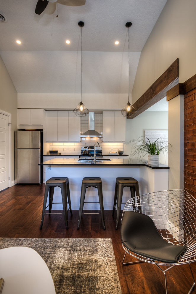 This is an example of an urban kitchen in Toronto with a double-bowl sink, flat-panel cabinets, white cabinets, granite worktops, white splashback, porcelain splashback, stainless steel appliances, medium hardwood flooring and an island.