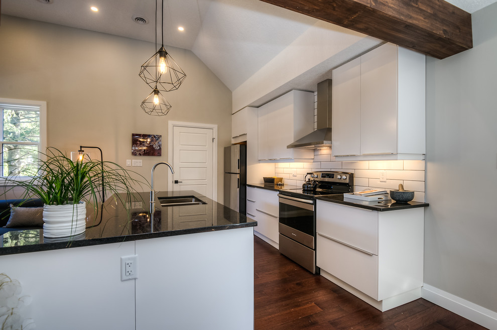 This is an example of an industrial kitchen in Toronto with a double-bowl sink, flat-panel cabinets, white cabinets, granite worktops, white splashback, porcelain splashback, stainless steel appliances, medium hardwood flooring and an island.
