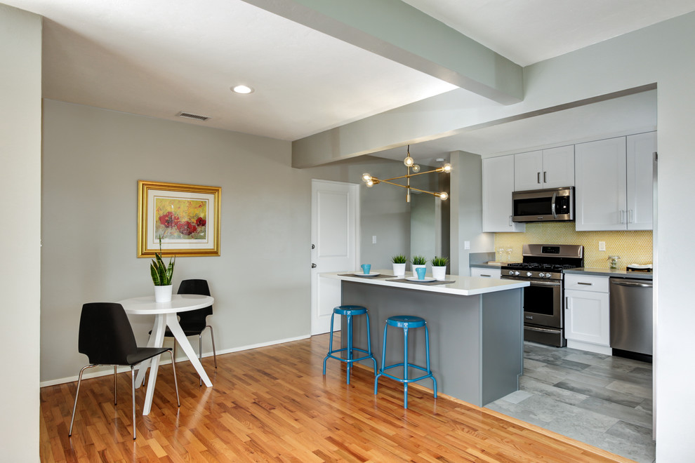 Small minimalist l-shaped porcelain tile open concept kitchen photo in San Diego with a drop-in sink, shaker cabinets, white cabinets, quartz countertops, yellow backsplash, mosaic tile backsplash, stainless steel appliances and an island