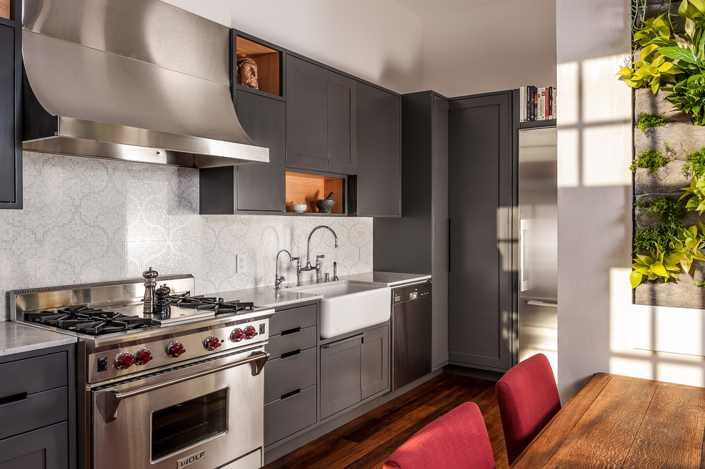 Bild på ett litet funkis linjärt kök och matrum, med en rustik diskho, släta luckor, grå skåp, stänkskydd med metallisk yta, rostfria vitvaror och mörkt trägolv
