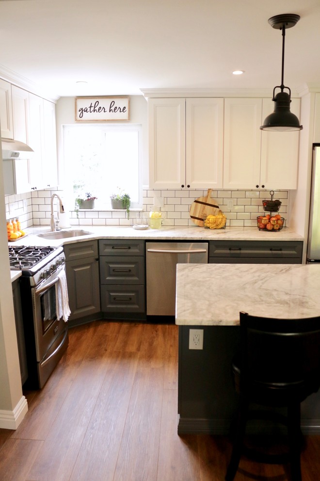 Foto på ett litet lantligt vit kök, med en undermonterad diskho, luckor med upphöjd panel, grå skåp, granitbänkskiva, vitt stänkskydd, stänkskydd i porslinskakel, rostfria vitvaror, laminatgolv, en köksö och brunt golv