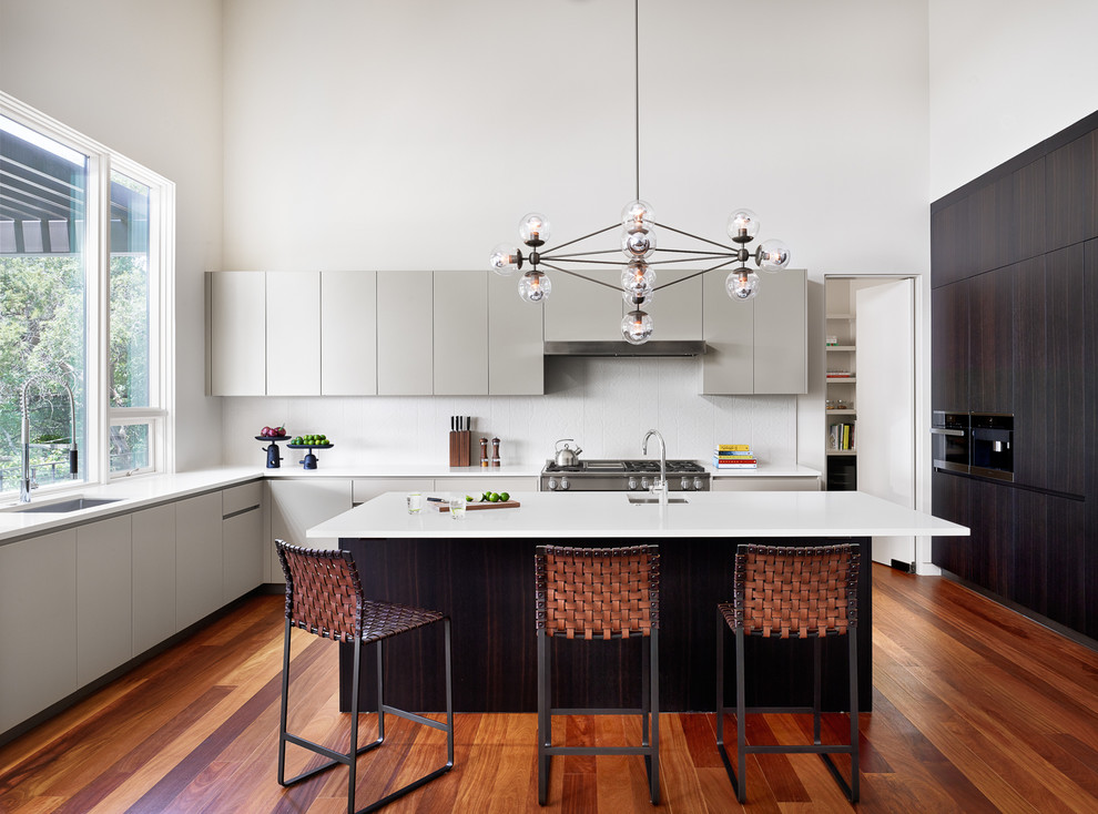Inspiration for a contemporary u-shaped open plan kitchen in Austin with a submerged sink, dark wood cabinets, engineered stone countertops, porcelain splashback, integrated appliances, medium hardwood flooring, an island and white splashback.