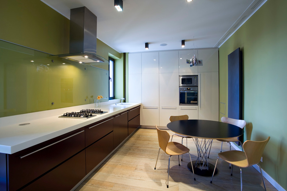 Moderne Wohnküche in L-Form mit flächenbündigen Schrankfronten, Glasrückwand und Küchengeräten aus Edelstahl in Sonstige