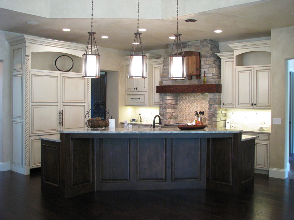 Rustik inredning av ett stort flerfärgad flerfärgat l-kök, med mörkt trägolv, brunt golv, en undermonterad diskho, luckor med upphöjd panel, vita skåp, granitbänkskiva, beige stänkskydd, stänkskydd i stenkakel, integrerade vitvaror och en köksö