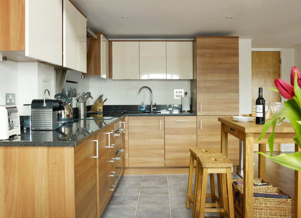 Small urban l-shaped porcelain tile eat-in kitchen photo in London with an undermount sink, flat-panel cabinets, medium tone wood cabinets, granite countertops, white backsplash, glass sheet backsplash, stainless steel appliances and an island
