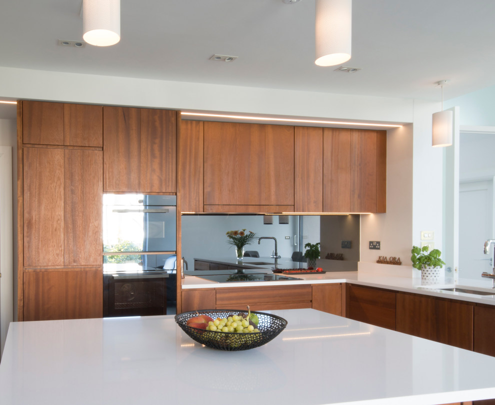 Photo of a medium sized contemporary l-shaped kitchen/diner in Dublin with a built-in sink, flat-panel cabinets, medium wood cabinets, engineered stone countertops, grey splashback, mirror splashback, stainless steel appliances, porcelain flooring and an island.
