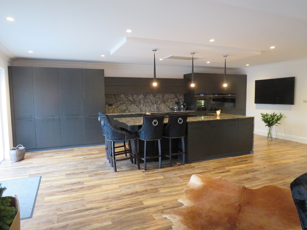 Design ideas for a large contemporary single-wall open plan kitchen in Essex with a built-in sink, flat-panel cabinets, black cabinets, quartz worktops, multi-coloured splashback, black appliances, dark hardwood flooring, an island, brown floors and multicoloured worktops.