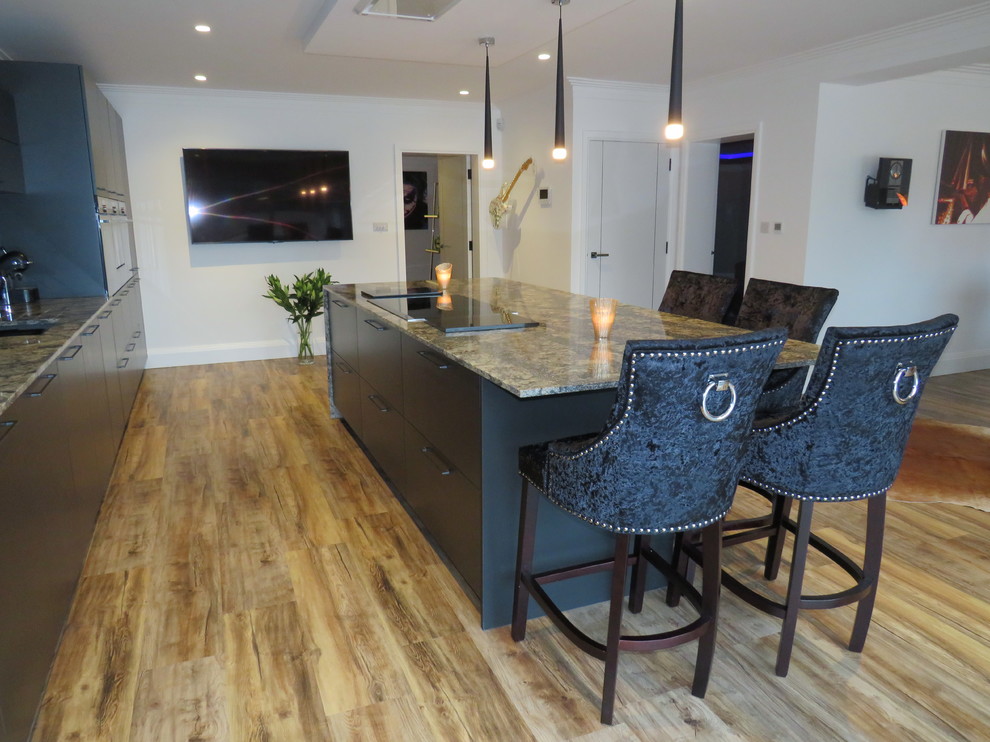 Large contemporary single-wall open plan kitchen in Essex with a built-in sink, flat-panel cabinets, black cabinets, quartz worktops, multi-coloured splashback, black appliances, dark hardwood flooring, an island, brown floors and multicoloured worktops.