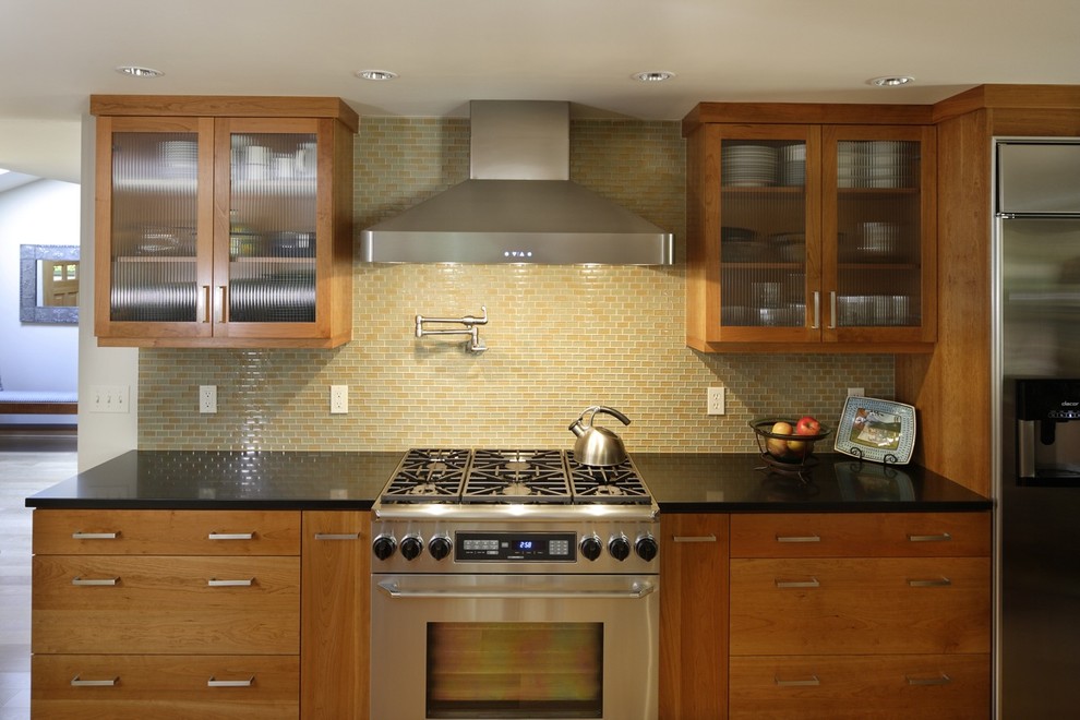 Example of a mid-sized trendy eat-in kitchen design in Portland with glass-front cabinets, glass tile backsplash, stainless steel appliances, medium tone wood cabinets and multicolored backsplash