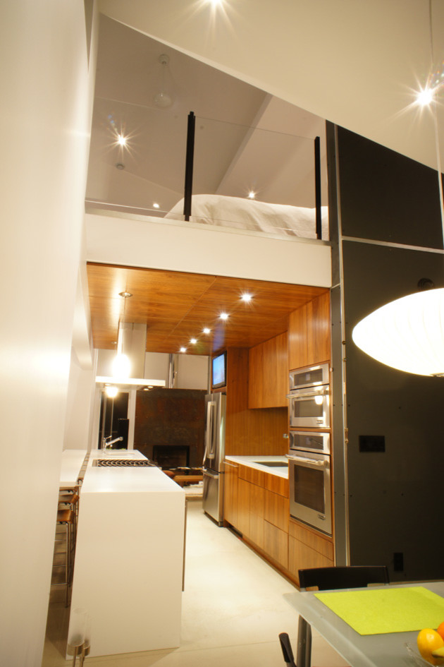 Modelo de cocina actual abierta con fregadero bajoencimera, armarios con paneles lisos, puertas de armario de madera oscura, encimera de acrílico y electrodomésticos de acero inoxidable