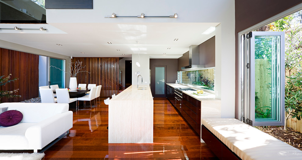 Modern inredning av ett linjärt kök med öppen planlösning, med en undermonterad diskho, släta luckor, svarta skåp, bänkskiva i kalksten, fönster som stänkskydd, rostfria vitvaror, mellanmörkt trägolv och en halv köksö