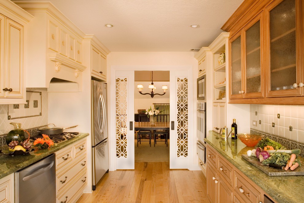 Enclosed kitchen - mid-sized traditional galley light wood floor enclosed kitchen idea in Orange County with a double-bowl sink, beaded inset cabinets, medium tone wood cabinets, granite countertops, green backsplash, ceramic backsplash, stainless steel appliances and no island