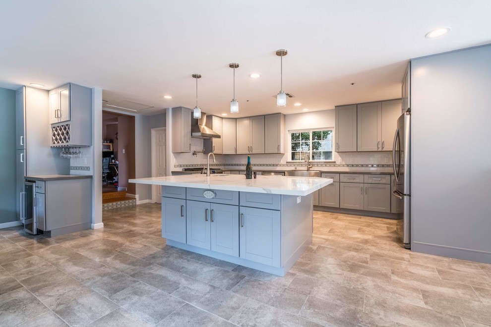 Inspiration for a mid-sized transitional u-shaped porcelain tile and gray floor eat-in kitchen remodel in Orange County with a farmhouse sink, recessed-panel cabinets, gray cabinets, quartz countertops, white backsplash, subway tile backsplash, stainless steel appliances, an island and white countertops