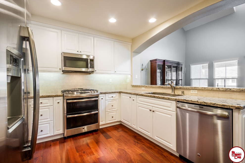 Small elegant galley medium tone wood floor enclosed kitchen photo in Orange County with an undermount sink, raised-panel cabinets, white cabinets, quartz countertops, white backsplash, stainless steel appliances and a peninsula