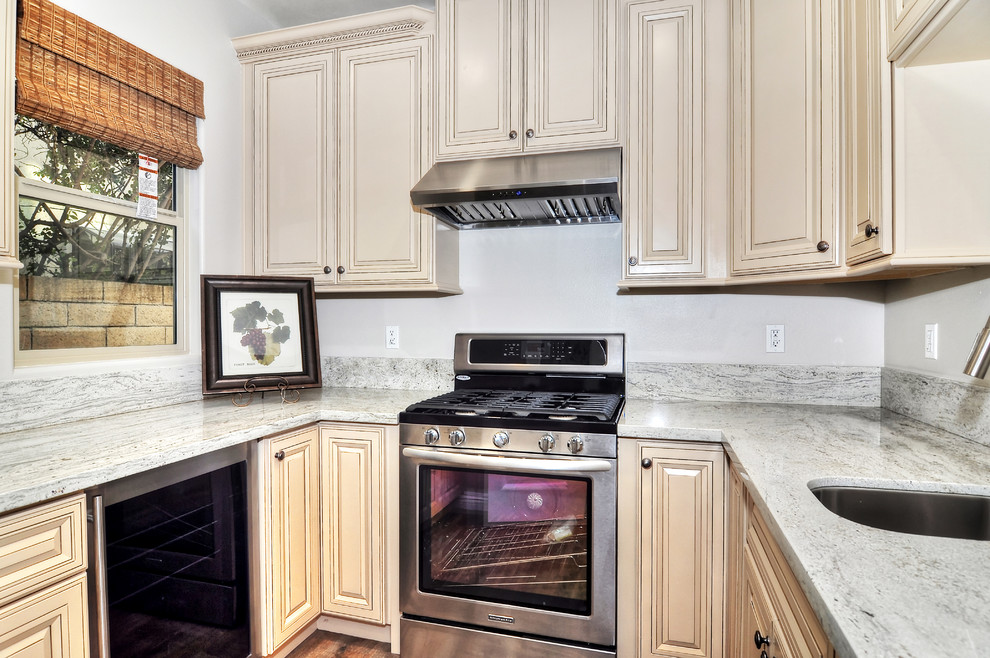 Exempel på ett avskilt, litet klassiskt u-kök, med en undermonterad diskho, granitbänkskiva, rostfria vitvaror, mellanmörkt trägolv, luckor med upphöjd panel och skåp i ljust trä
