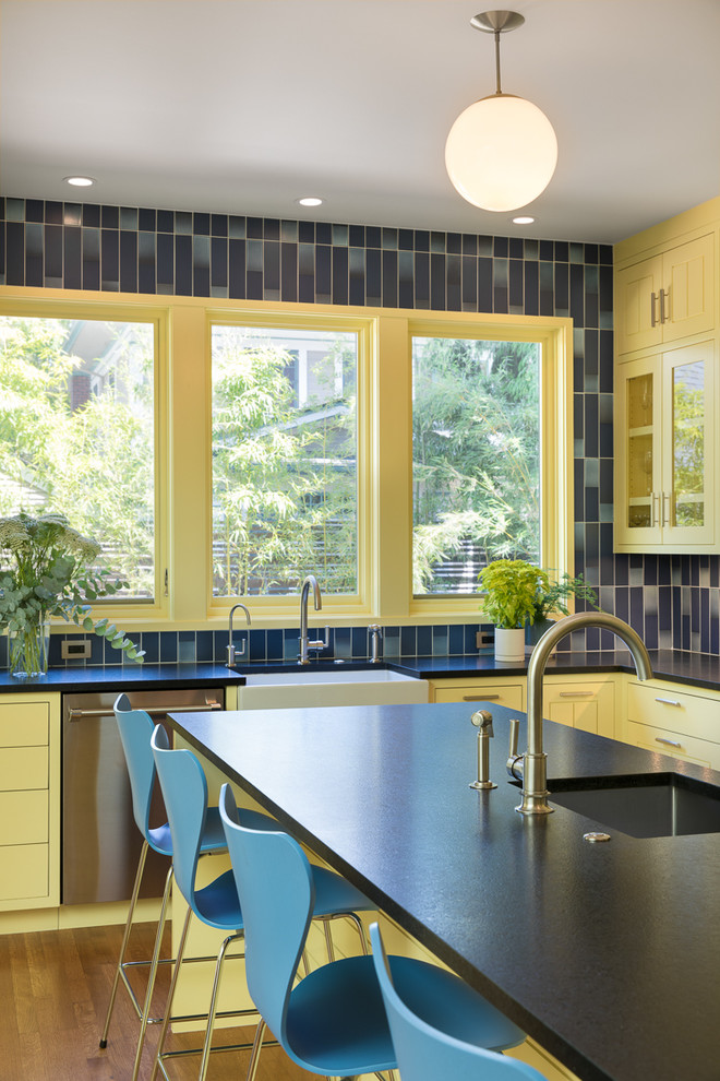 ポートランドにある高級な広い北欧スタイルのおしゃれなキッチン (エプロンフロントシンク、ガラス扉のキャビネット、黄色いキャビネット、御影石カウンター、青いキッチンパネル、セラミックタイルのキッチンパネル、シルバーの調理設備、淡色無垢フローリング、黒いキッチンカウンター) の写真