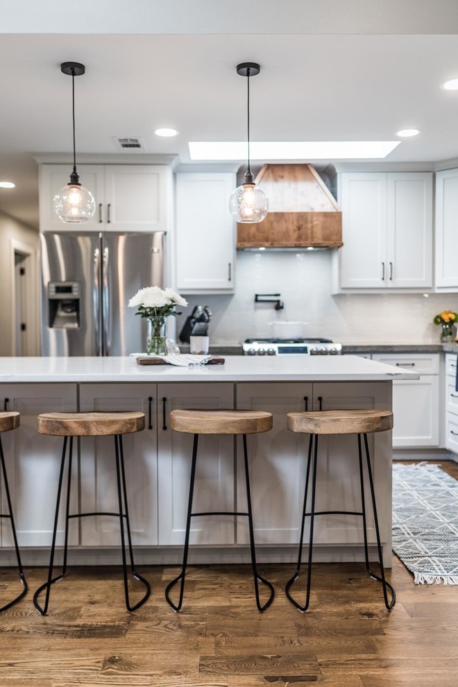 Inspiration for a mid-sized farmhouse l-shaped medium tone wood floor and brown floor open concept kitchen remodel in Dallas with a farmhouse sink, shaker cabinets, white cabinets, concrete countertops, white backsplash, ceramic backsplash, stainless steel appliances, an island and gray countertops