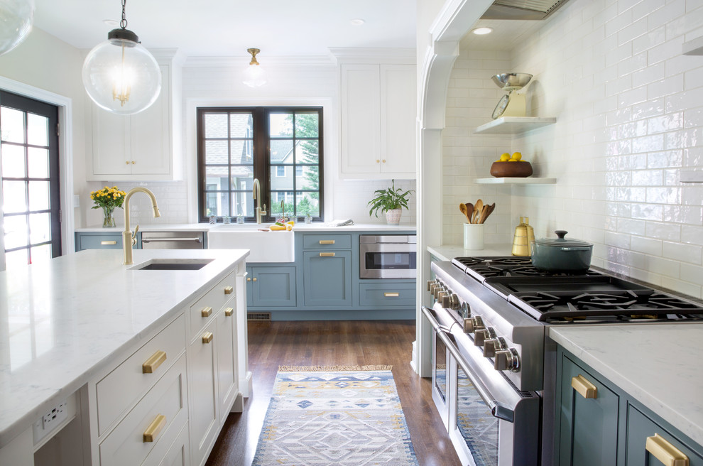 Inspiration for a medium sized classic l-shaped enclosed kitchen in New York with a belfast sink, shaker cabinets, white cabinets, engineered stone countertops, white splashback, ceramic splashback, stainless steel appliances, dark hardwood flooring, an island, brown floors and white worktops.