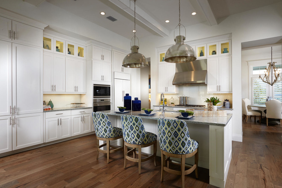 Traditional l-shaped kitchen in Tampa with shaker cabinets, white cabinets, white splashback, stainless steel appliances, dark hardwood flooring and an island.