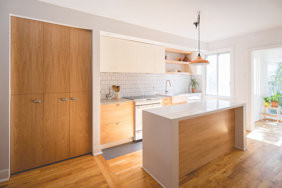 This is an example of a medium sized contemporary galley kitchen/diner in Montreal with a single-bowl sink, flat-panel cabinets, medium wood cabinets, tile countertops, white splashback, ceramic splashback, white appliances, ceramic flooring, an island and grey floors.