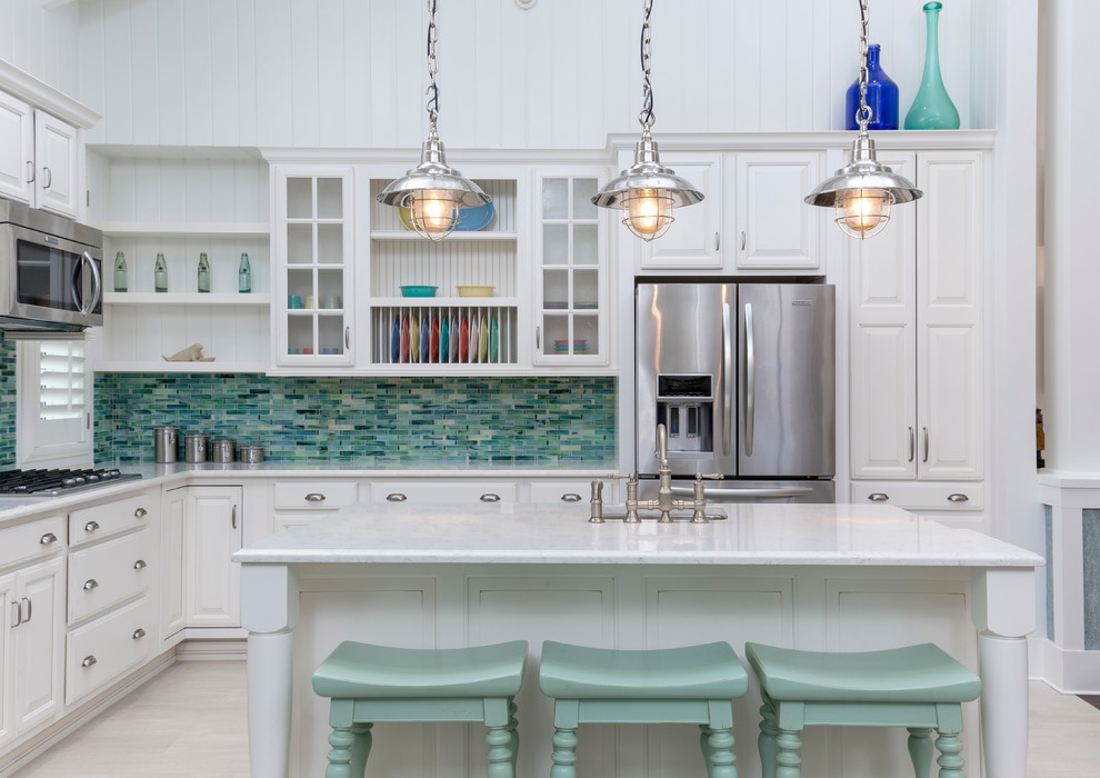 Foto på ett maritimt l-kök, med en undermonterad diskho, luckor med upphöjd panel, vita skåp, grönt stänkskydd, stänkskydd i mosaik, rostfria vitvaror och en köksö