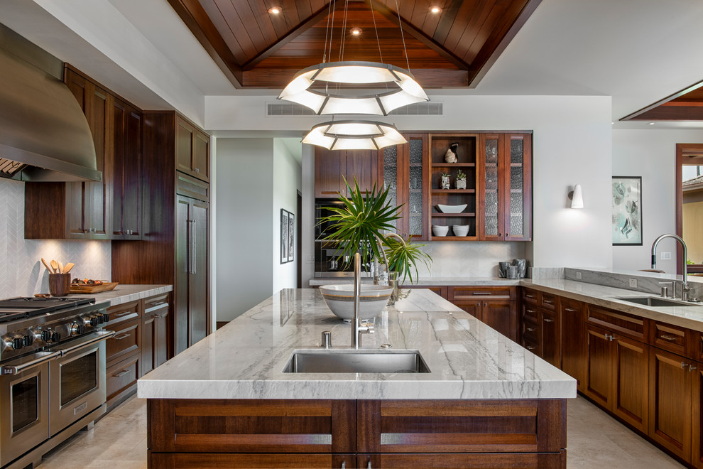 Photo of a world-inspired u-shaped kitchen in Hawaii with a submerged sink, recessed-panel cabinets, medium wood cabinets, grey splashback, stainless steel appliances, an island, beige floors and grey worktops.