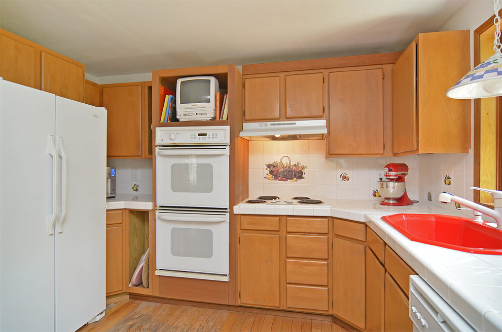 Bild på ett mellanstort lantligt kök, med en nedsänkt diskho, släta luckor, skåp i mellenmörkt trä, kaklad bänkskiva, gult stänkskydd, stänkskydd i keramik, vita vitvaror, mellanmörkt trägolv och en köksö