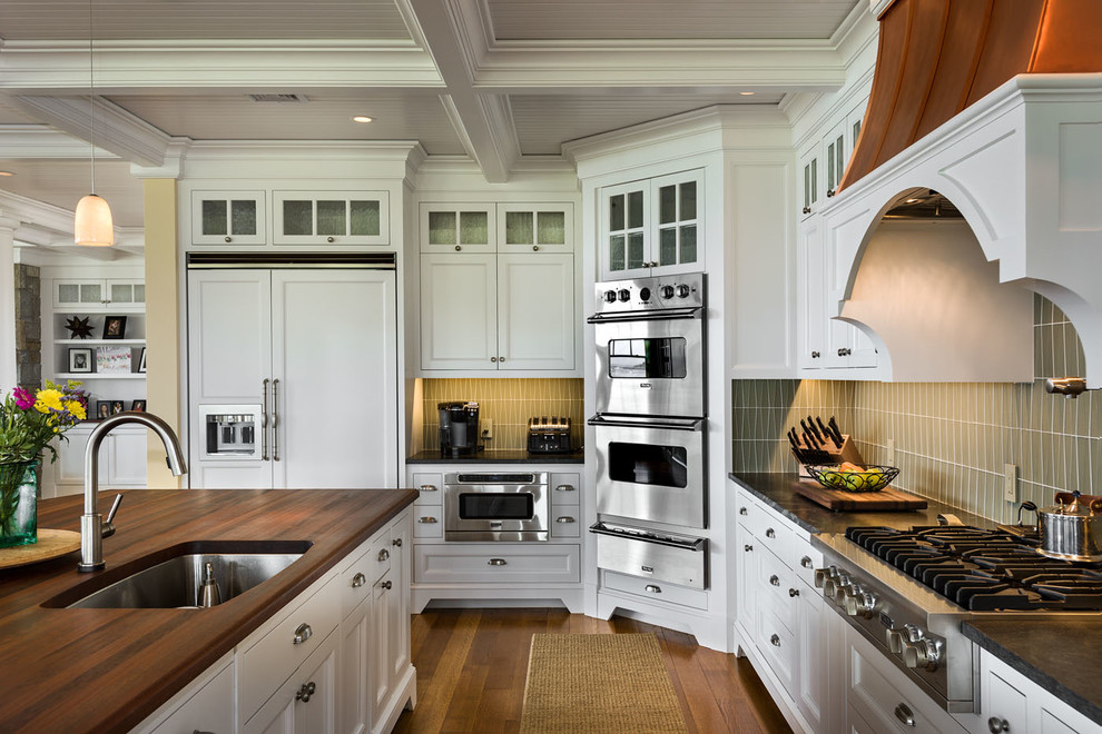 Large coastal l-shaped kitchen/diner in Boston with a submerged sink, recessed-panel cabinets, white cabinets, granite worktops, green splashback, stainless steel appliances, medium hardwood flooring and an island.