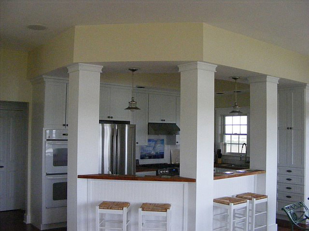 Ejemplo de cocinas en U costero de tamaño medio abierto con armarios con rebordes decorativos, puertas de armario blancas y encimera de madera