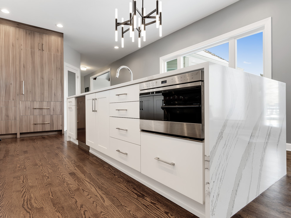 Inspiration for a large modern l-shaped medium tone wood floor and brown floor enclosed kitchen remodel in Chicago with an undermount sink, flat-panel cabinets, white cabinets, quartz countertops, gray backsplash, porcelain backsplash, paneled appliances, an island and white countertops