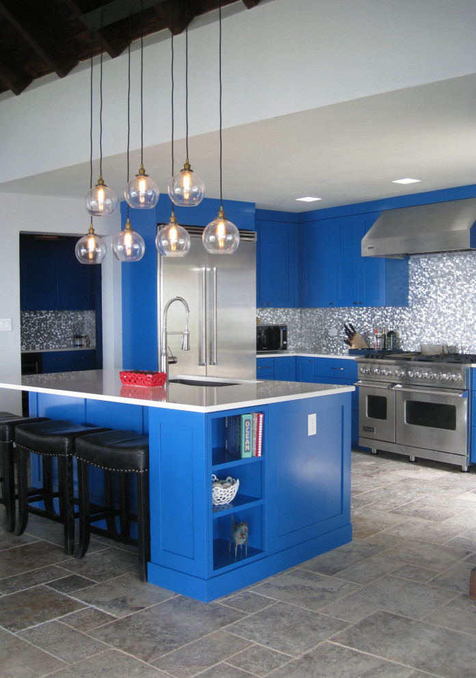 他の地域にある高級な中くらいなトロピカルスタイルのおしゃれなキッチン (シングルシンク、落し込みパネル扉のキャビネット、青いキャビネット、人工大理石カウンター、メタリックのキッチンパネル、メタルタイルのキッチンパネル、シルバーの調理設備、磁器タイルの床、グレーの床、白いキッチンカウンター) の写真