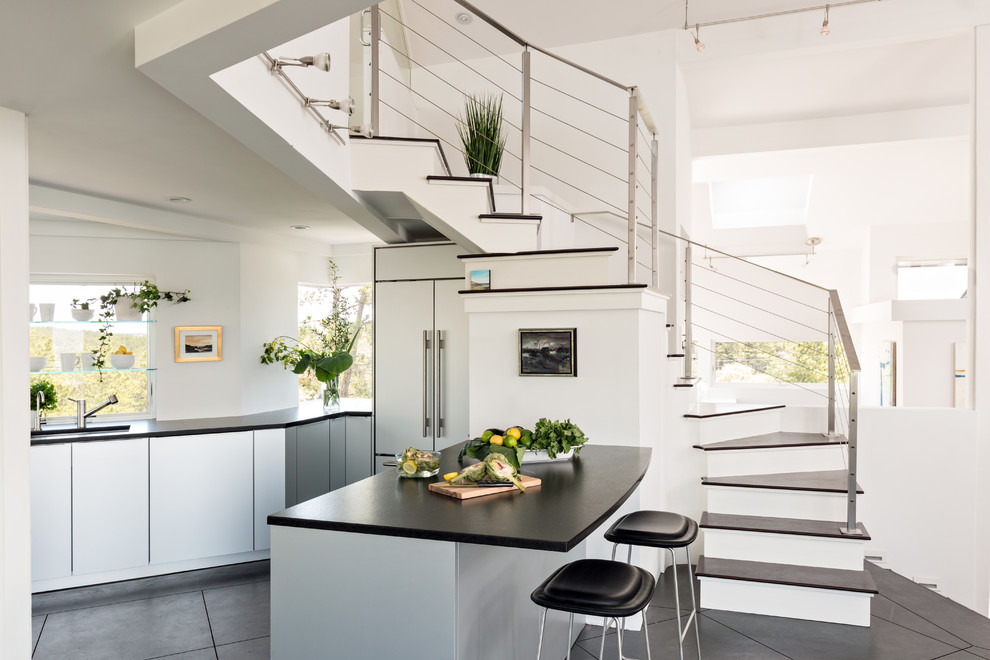 Diseño de cocina comedor costera con fregadero bajoencimera, armarios con paneles lisos, suelo de cemento, puertas de armario grises, encimera de cemento, electrodomésticos de acero inoxidable y una isla