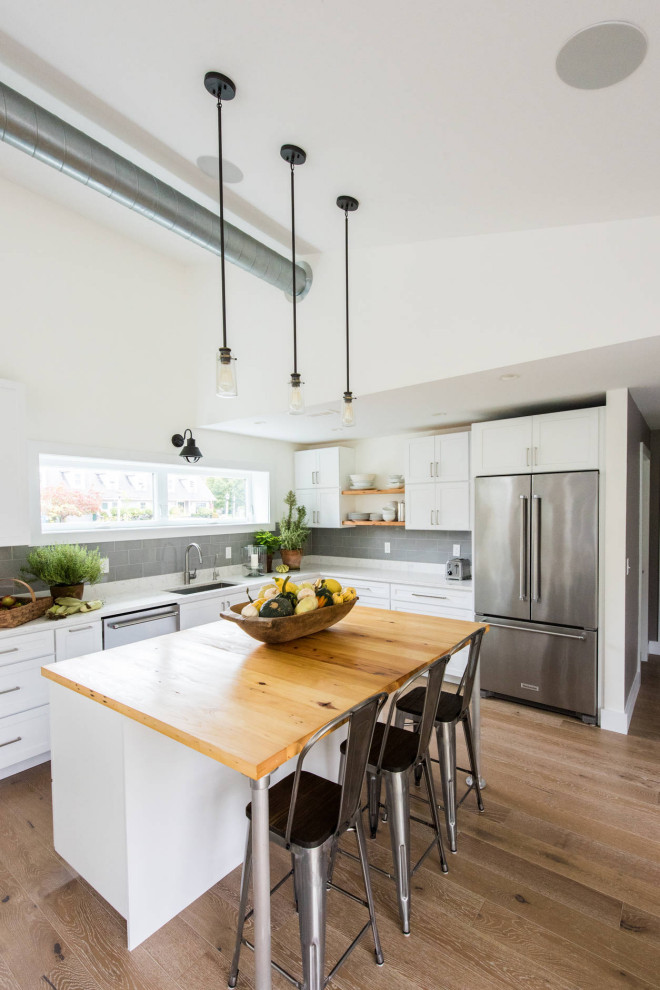 Exempel på ett mellanstort industriellt vit vitt kök, med en undermonterad diskho, skåp i shakerstil, vita skåp, bänkskiva i kvarts, grått stänkskydd, stänkskydd i glaskakel, rostfria vitvaror, ljust trägolv, en köksö och brunt golv