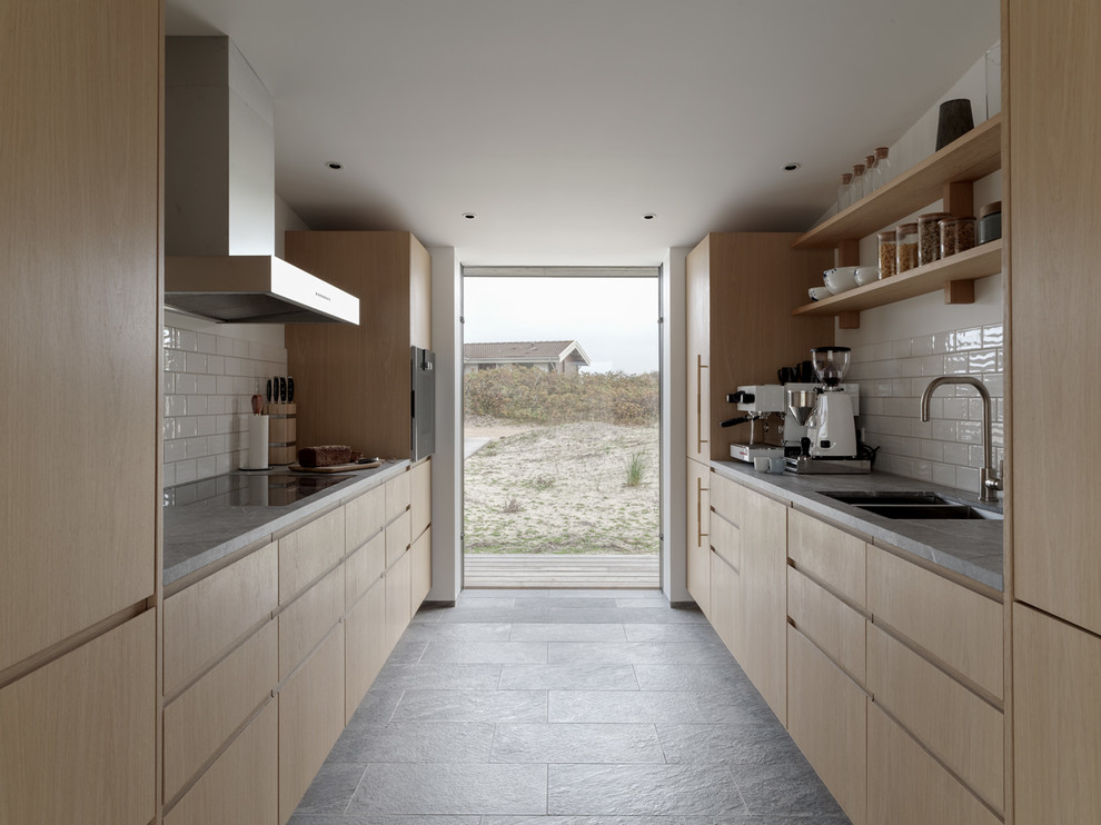 This is an example of a medium sized scandinavian galley open plan kitchen in London with a built-in sink, flat-panel cabinets, light wood cabinets, granite worktops, white splashback, porcelain splashback, stainless steel appliances, porcelain flooring, no island, grey floors and grey worktops.