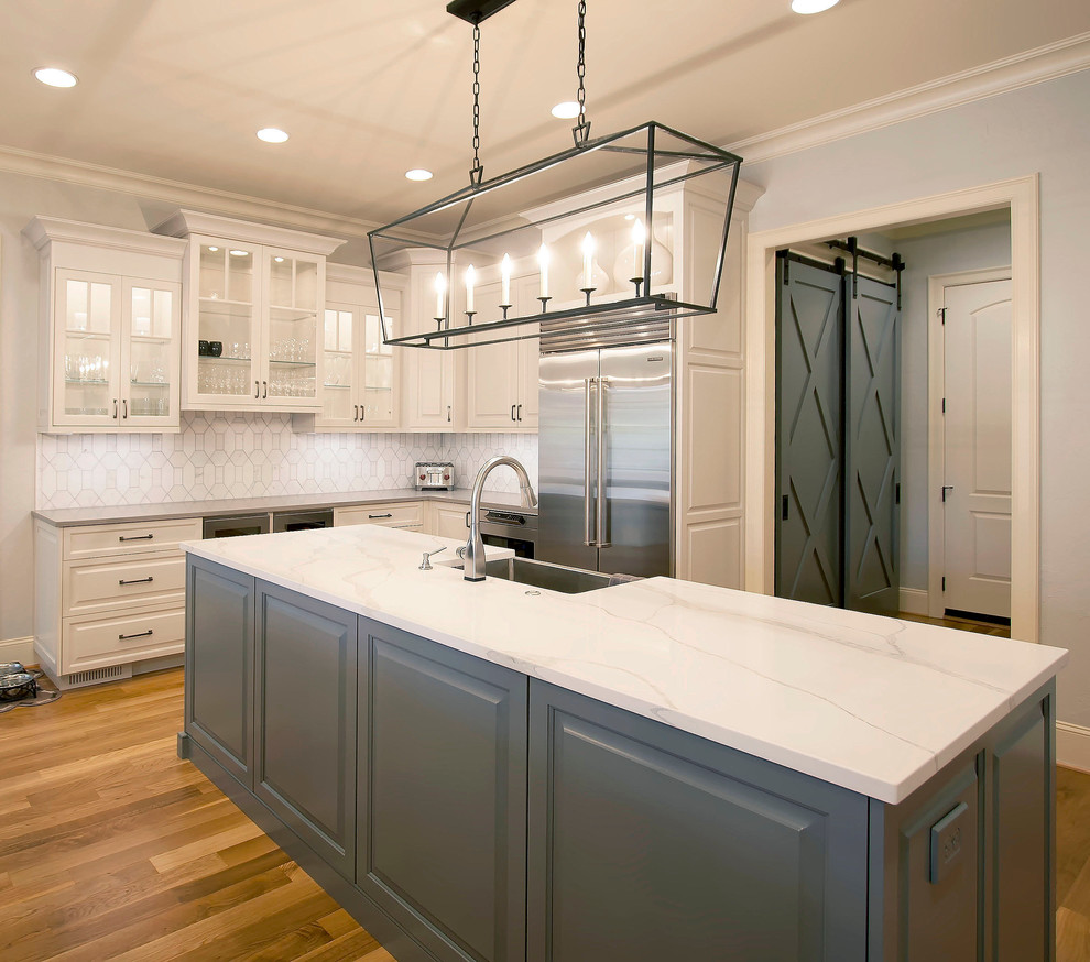 Inspiration for a large transitional medium tone wood floor eat-in kitchen remodel in Charlotte with a farmhouse sink, raised-panel cabinets, white cabinets, quartzite countertops, white backsplash, brick backsplash, stainless steel appliances and two islands