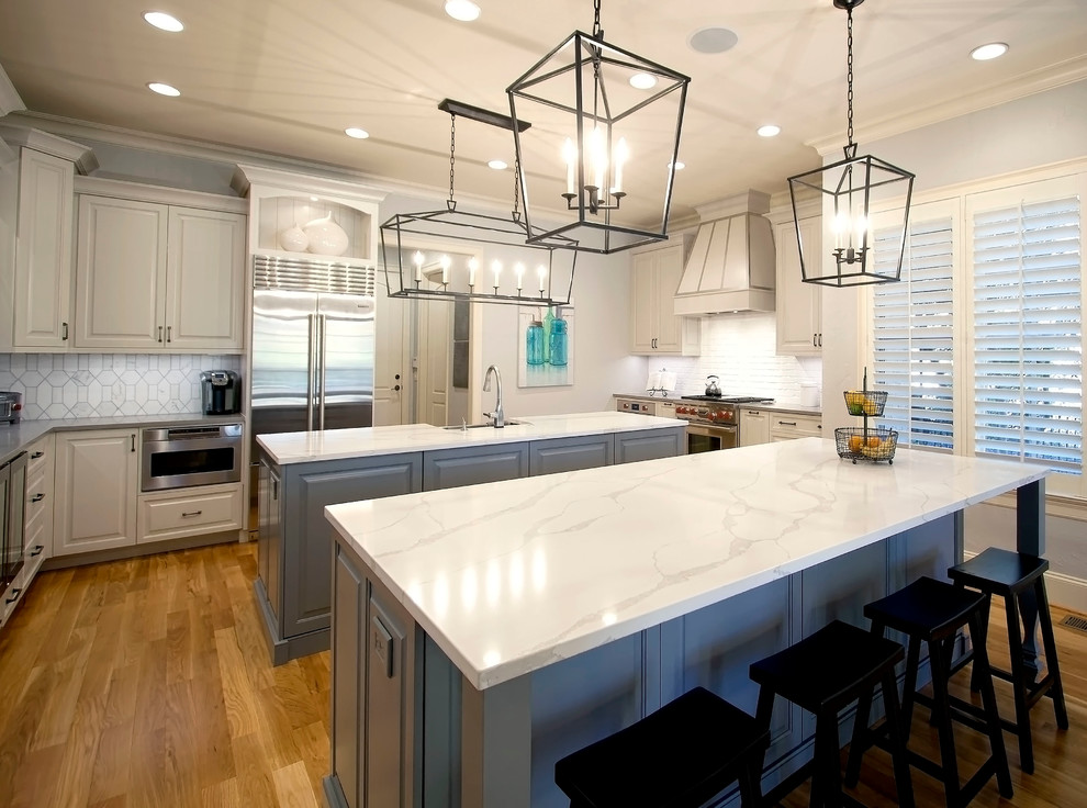 Large transitional medium tone wood floor eat-in kitchen photo in Charlotte with a farmhouse sink, raised-panel cabinets, white cabinets, quartzite countertops, white backsplash, brick backsplash, stainless steel appliances and two islands