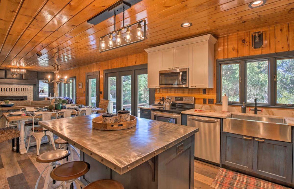 Idéer för ett mellanstort rustikt grå kök, med en rustik diskho, luckor med infälld panel, grå skåp, bänkskiva i rostfritt stål, rostfria vitvaror, mellanmörkt trägolv, en köksö och brunt golv