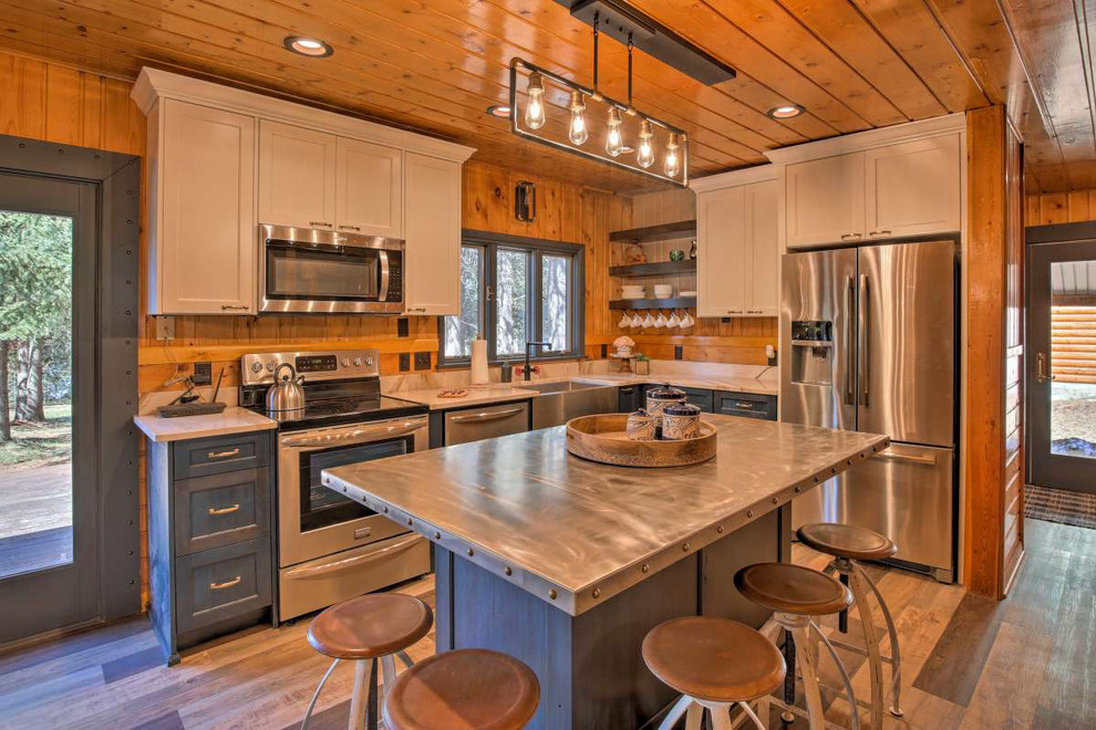 Mittelgroße Rustikale Küche in L-Form mit Landhausspüle, Schrankfronten mit vertiefter Füllung, grauen Schränken, Edelstahl-Arbeitsplatte, braunem Holzboden, Kücheninsel, braunem Boden und grauer Arbeitsplatte in Boise